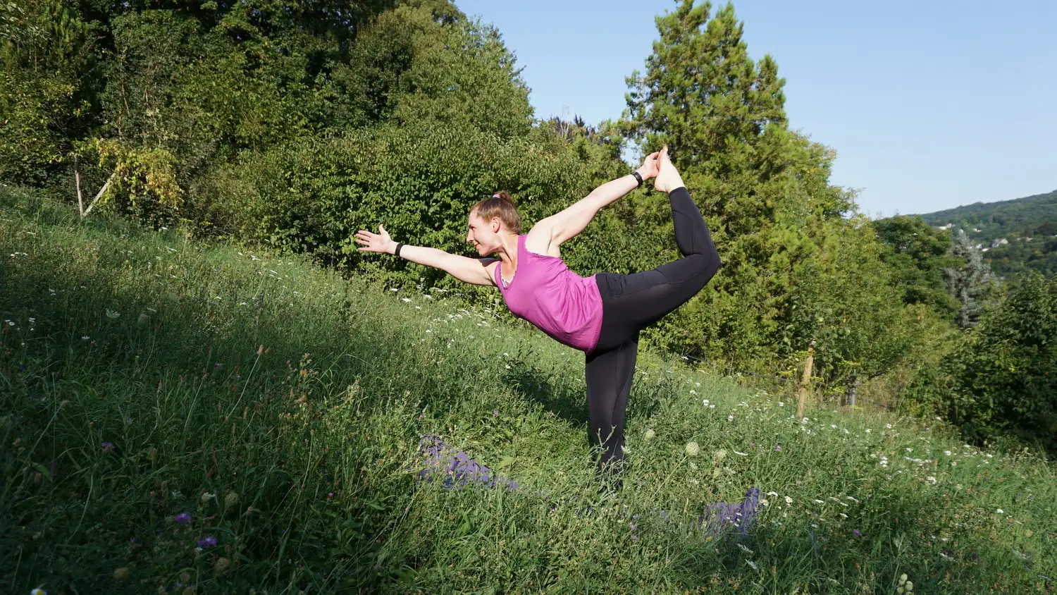 Marion steht auf einer Blumenwiese und macht Yoga.